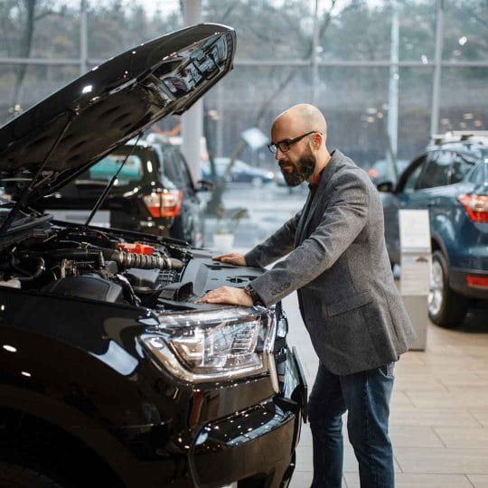 man at new truck with opened hood car dealership